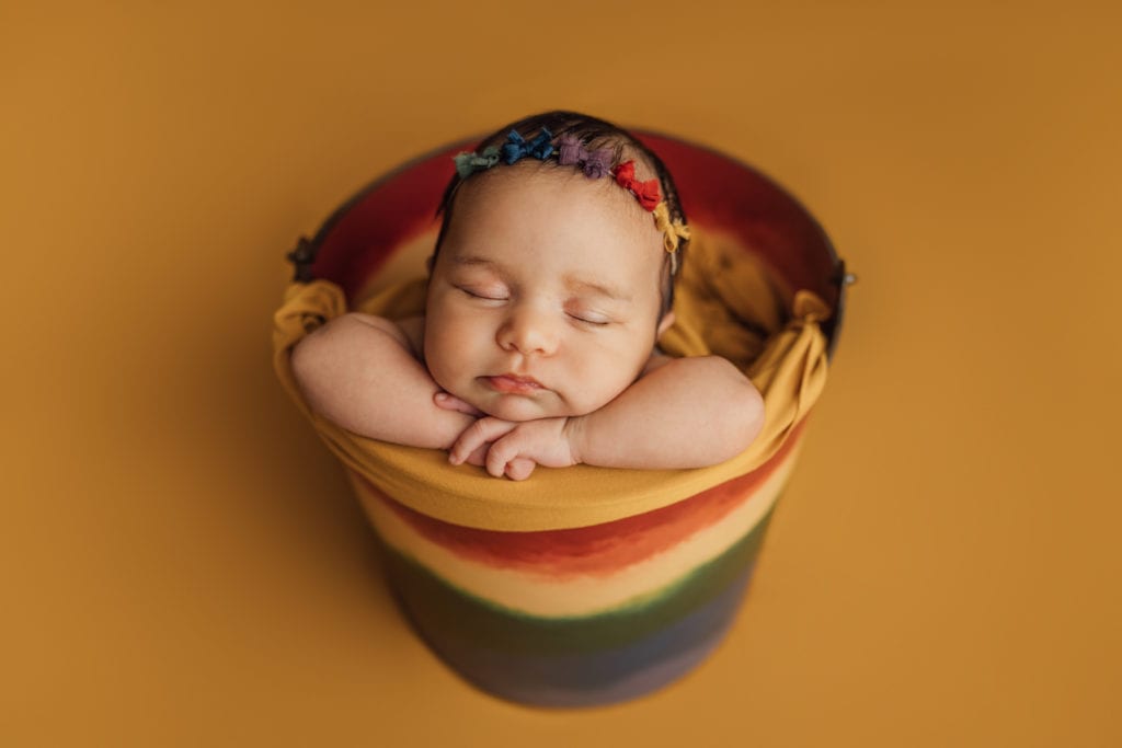 baby girl posed in rainbow bucket prop during newborn session in Tampa